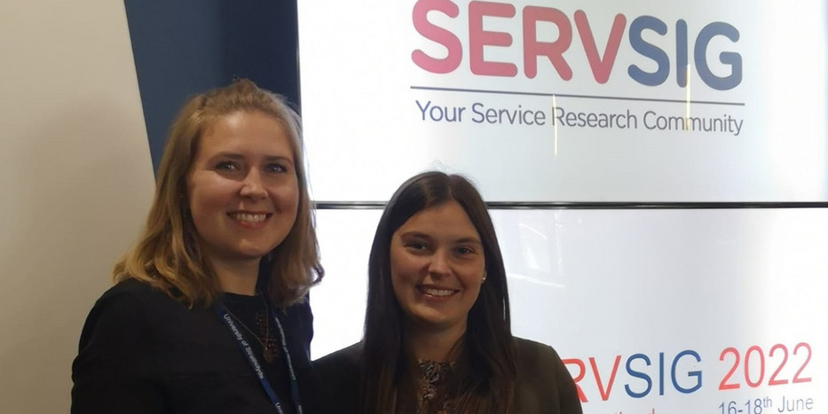 Xenia Raufeisen und Jana Grothaus (von links) vor einem Banner der SERVSIG Konferenz 2022