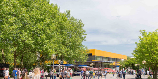 Mehrere Studierende stehen vor dem Mensagebäude und rechts sind grüne Bäume im Sommer.
